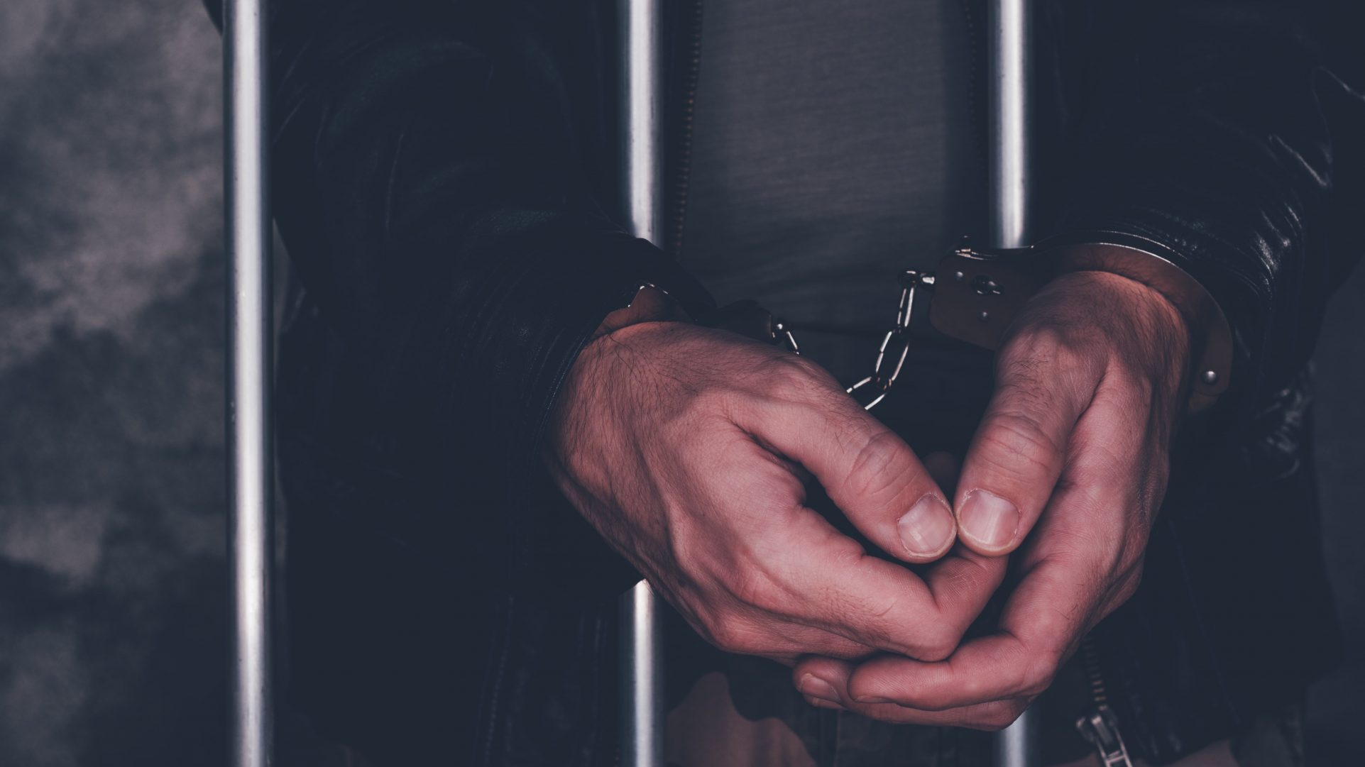 handcuffed-man-behind-prison-bars-P72M489-min