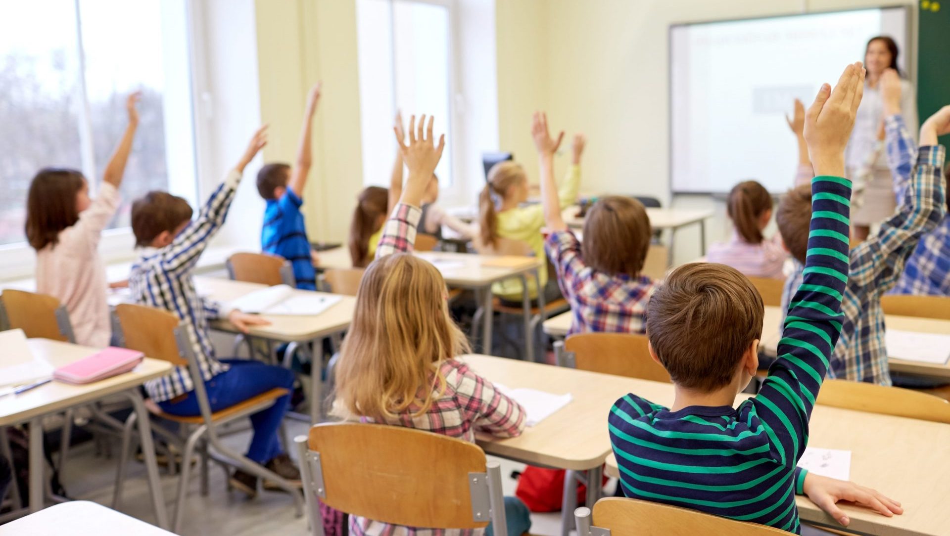 group-of-school-kids-raising-hands-in-classroom-PF36XQ9-min