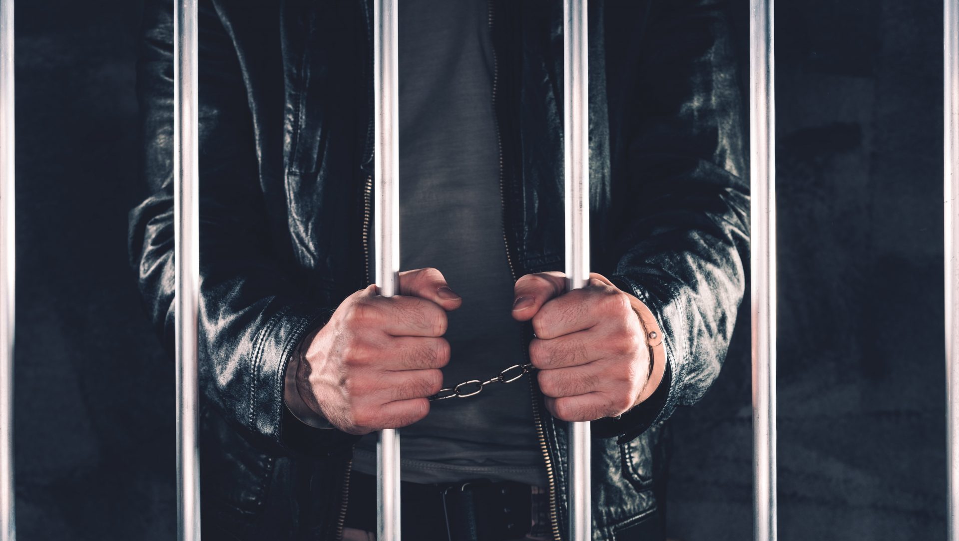 handcuffed-man-behind-prison-bars-P4RABNL-min