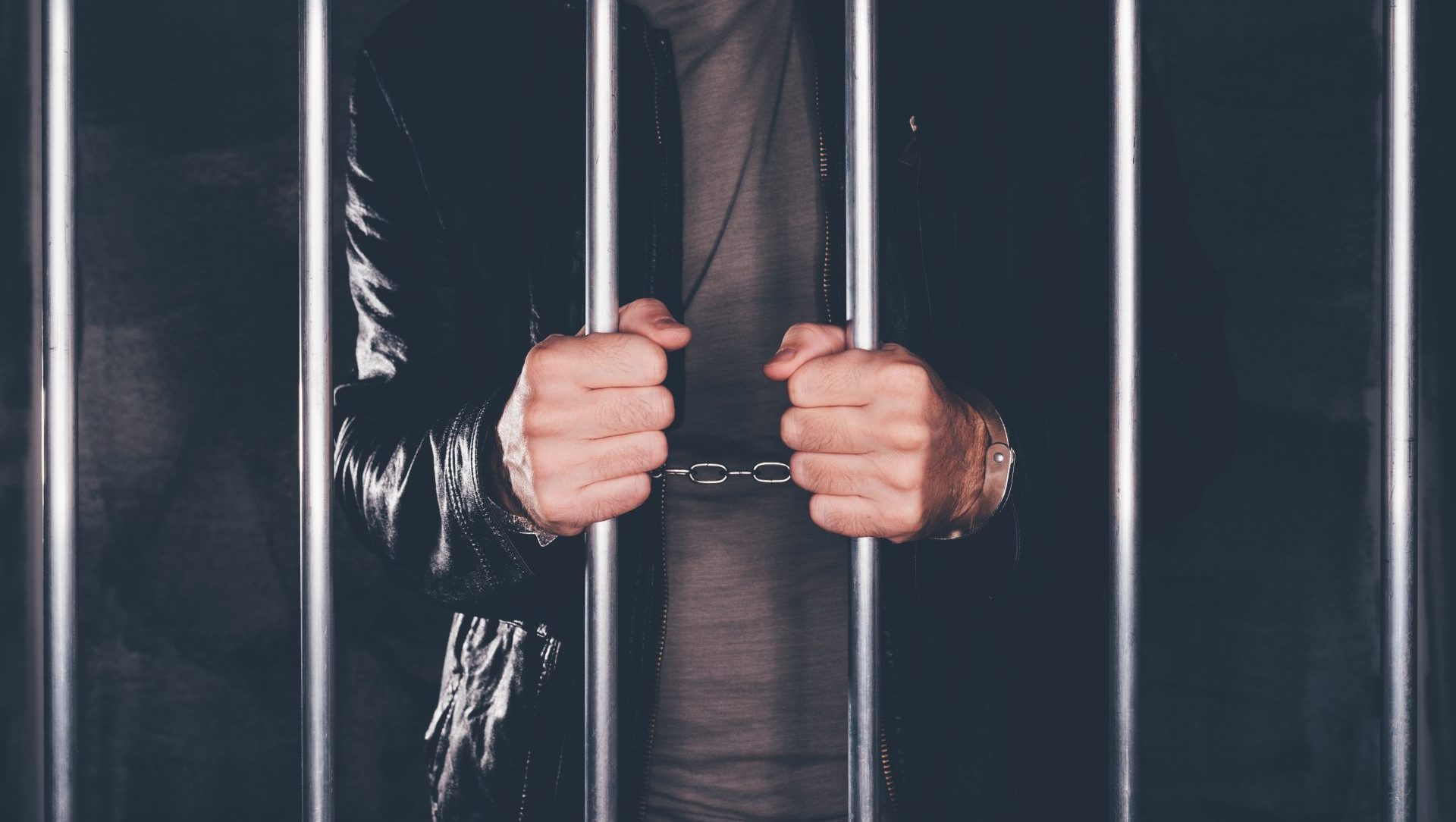 handcuffed-man-behind-prison-bars-PCYKQVJ-min