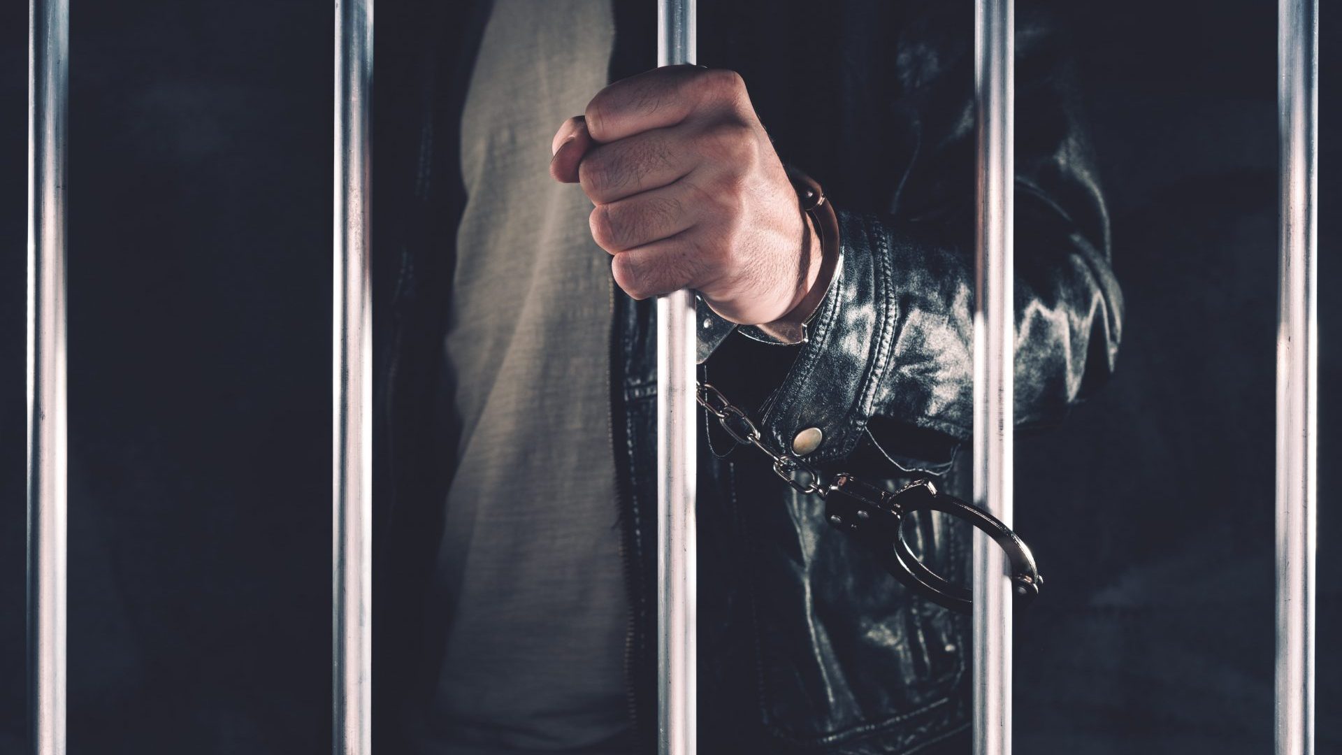 handcuffed-man-behind-prison-bars-PUKG9JP-min